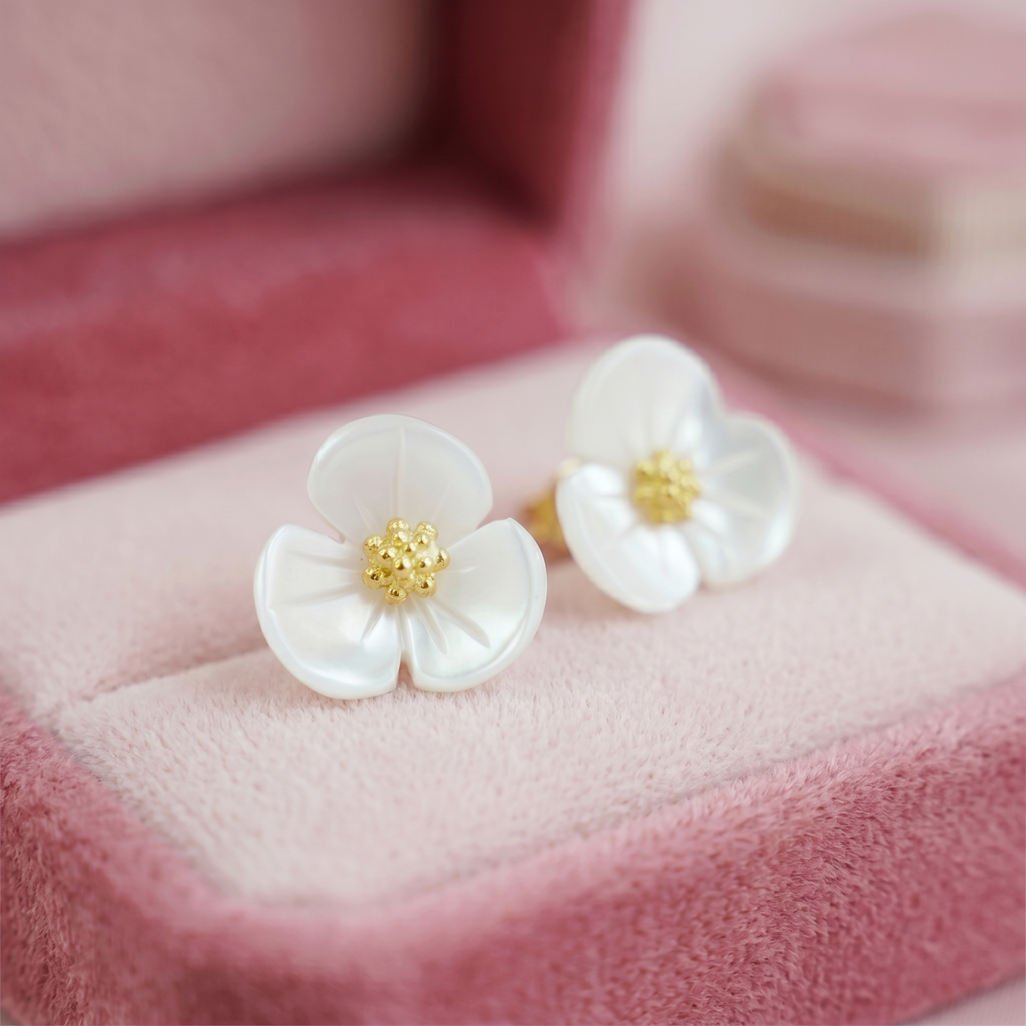 Close-up of white flower stud earrings with gold-tone center on pink fabric