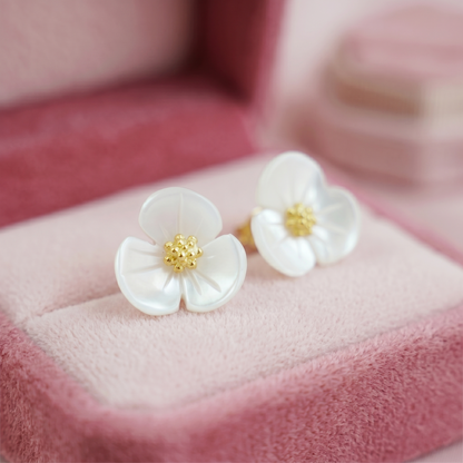 Close-up of white flower stud earrings with gold-tone center on pink fabric