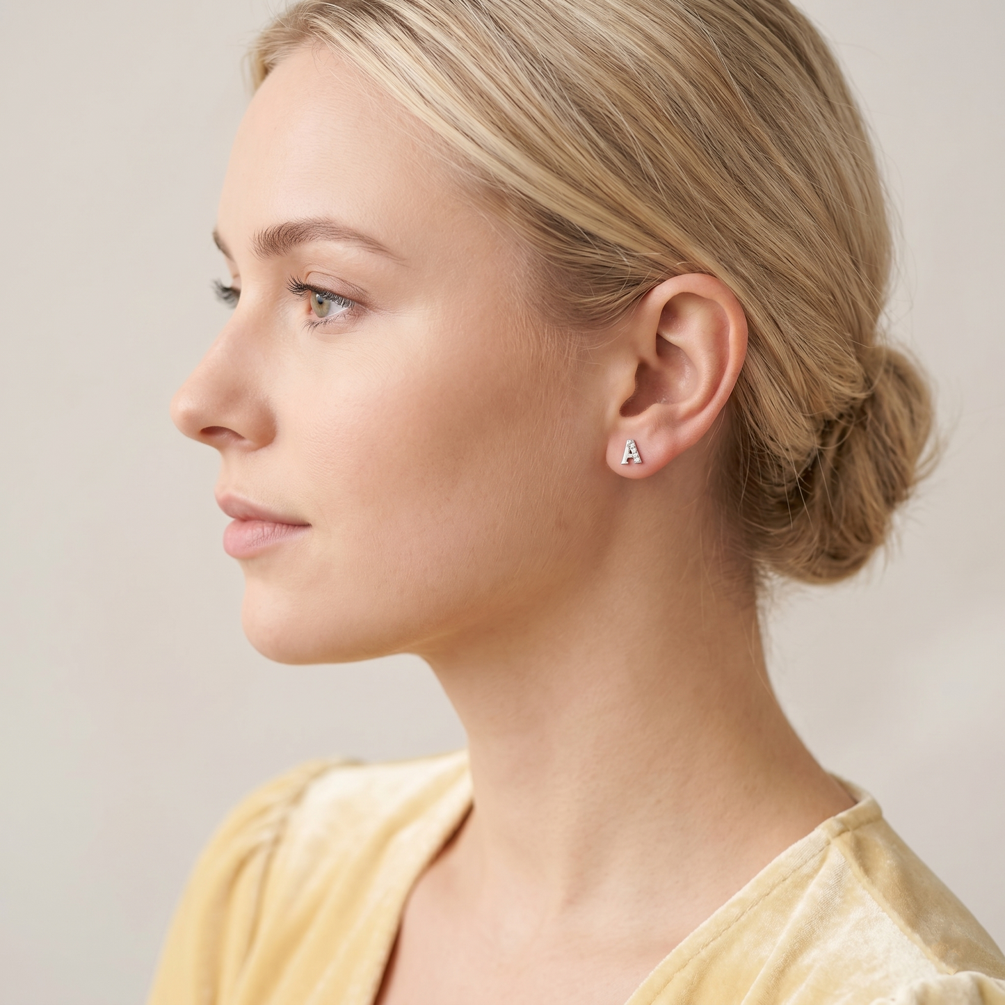 Paved initial stud earring letter A in silver-tone on the ear.