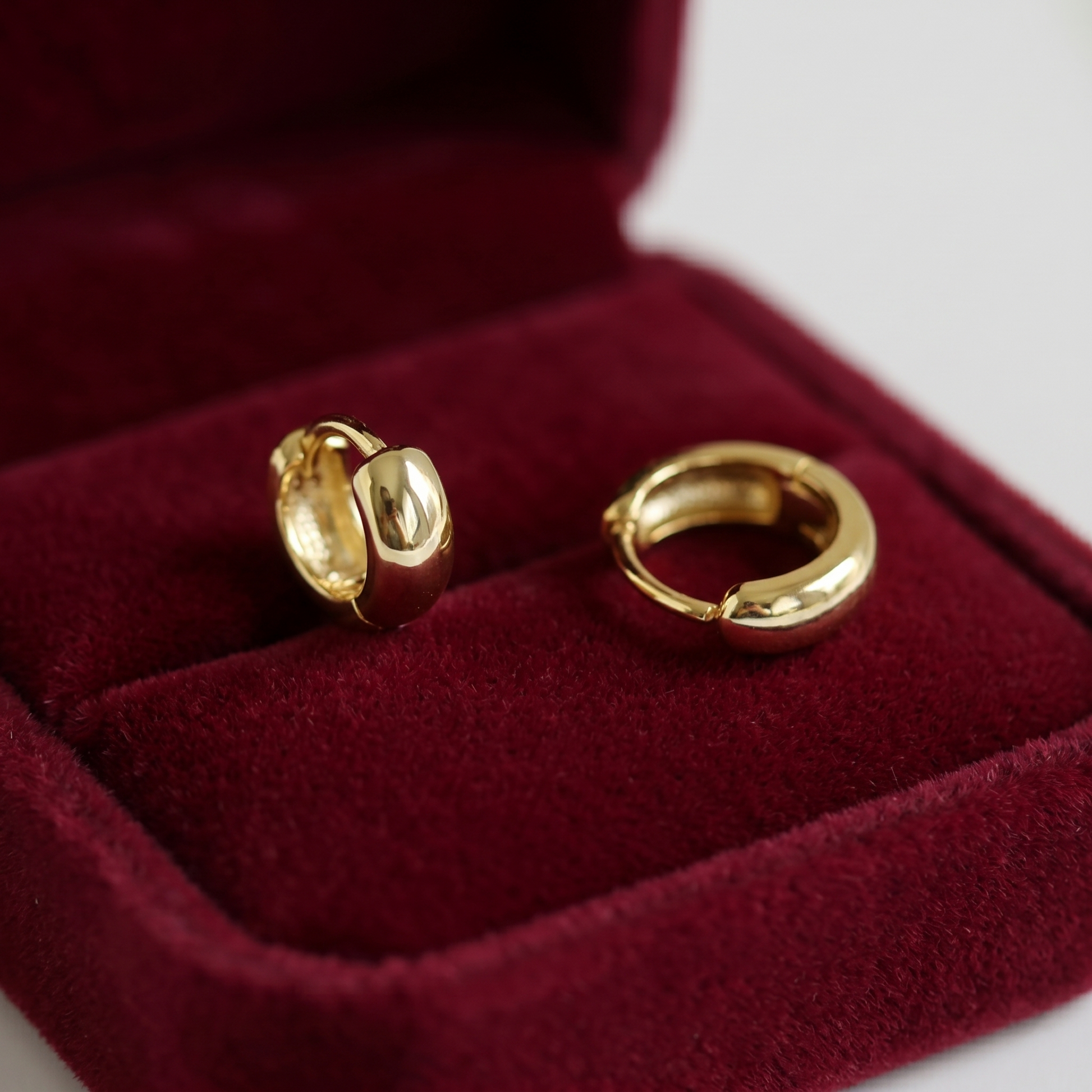 Gold sleeper huggie earrings, close-up in red velvet