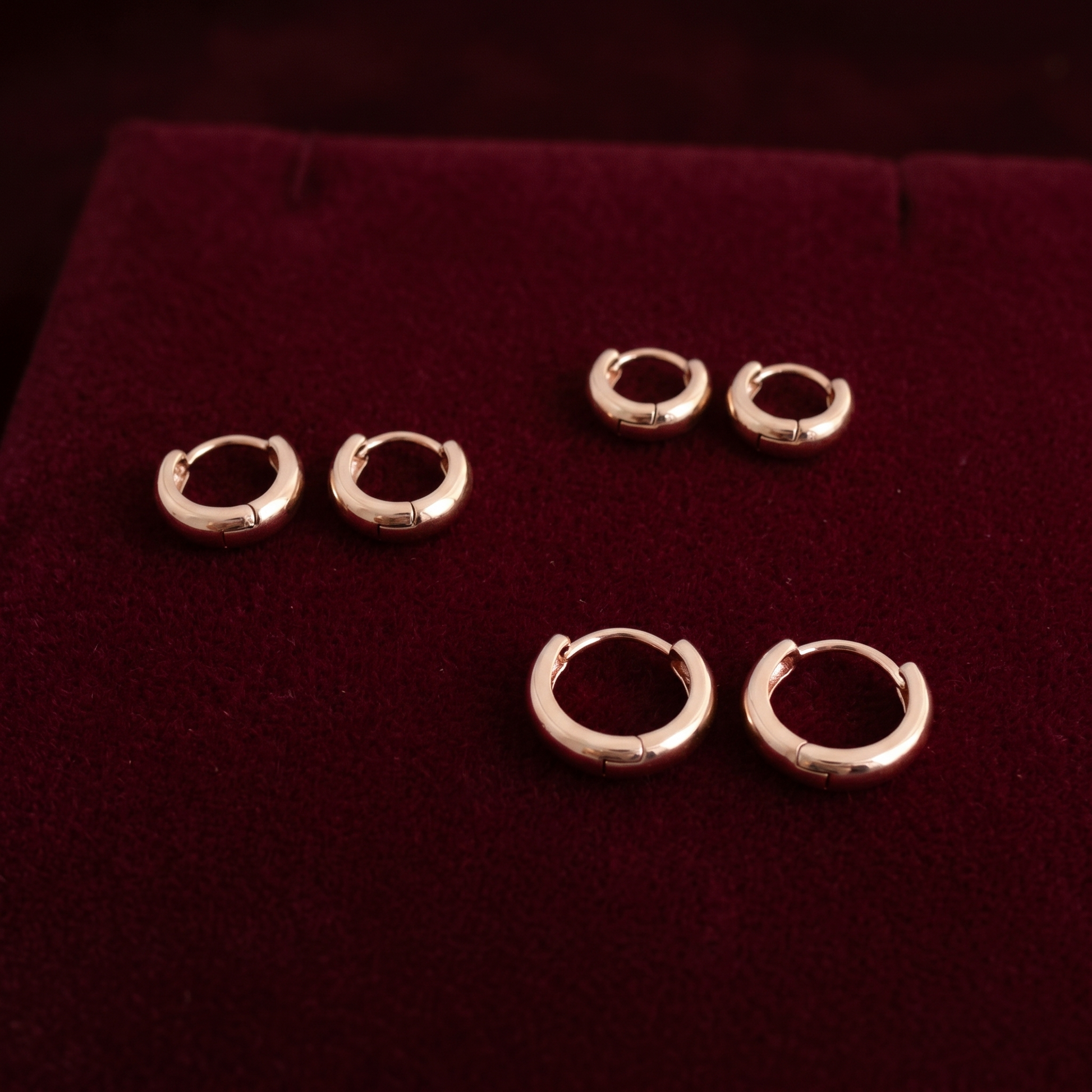 Gold-tone bold huggie hoop earrings displayed on dark velvet