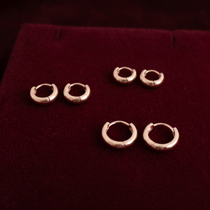 Gold-tone bold huggie hoop earrings displayed on dark velvet