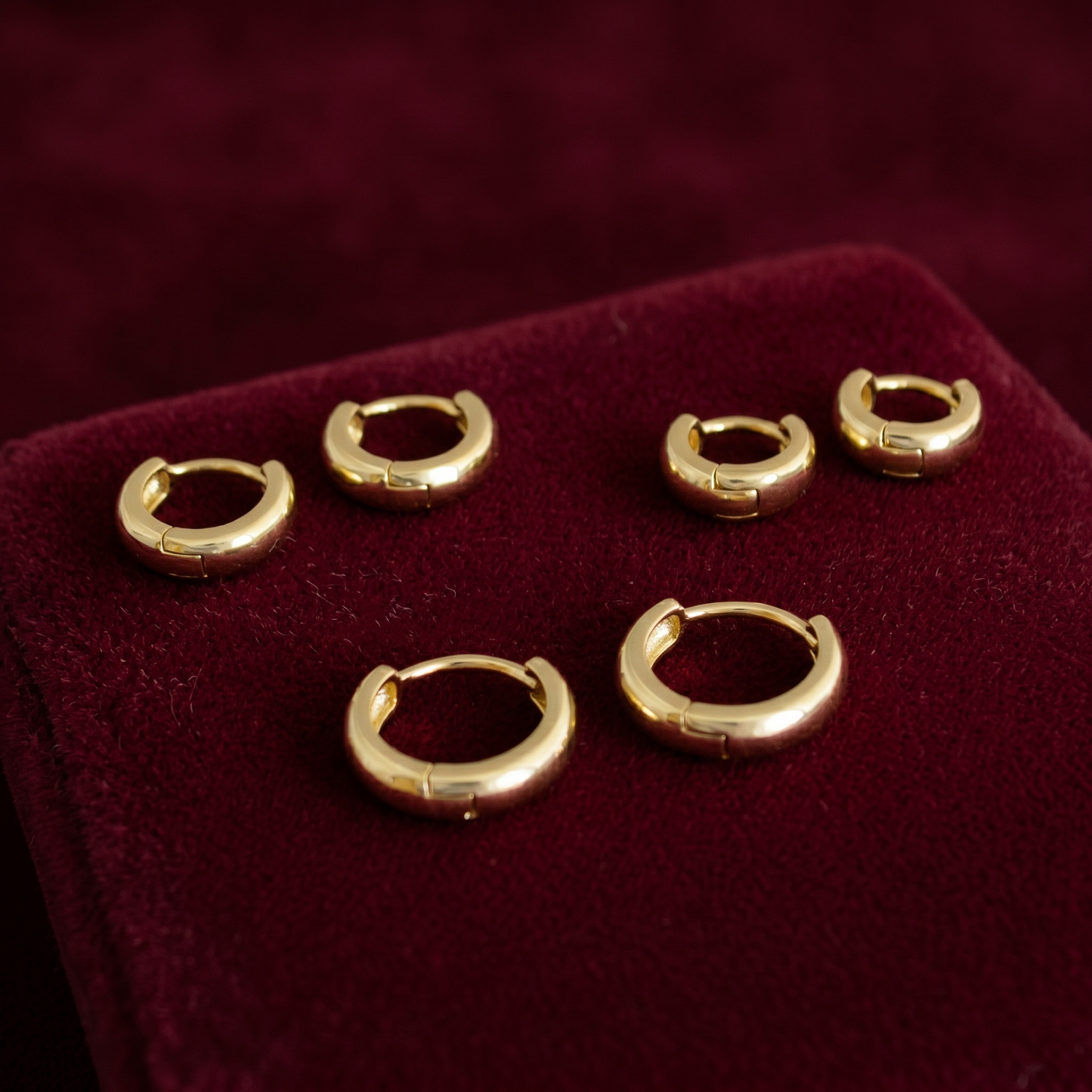 Gold sleeper huggie earrings on red velvet display