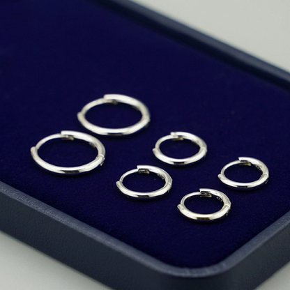 Rhodium-tone huggie hoop earrings with hinged closure, several pairs arranged
