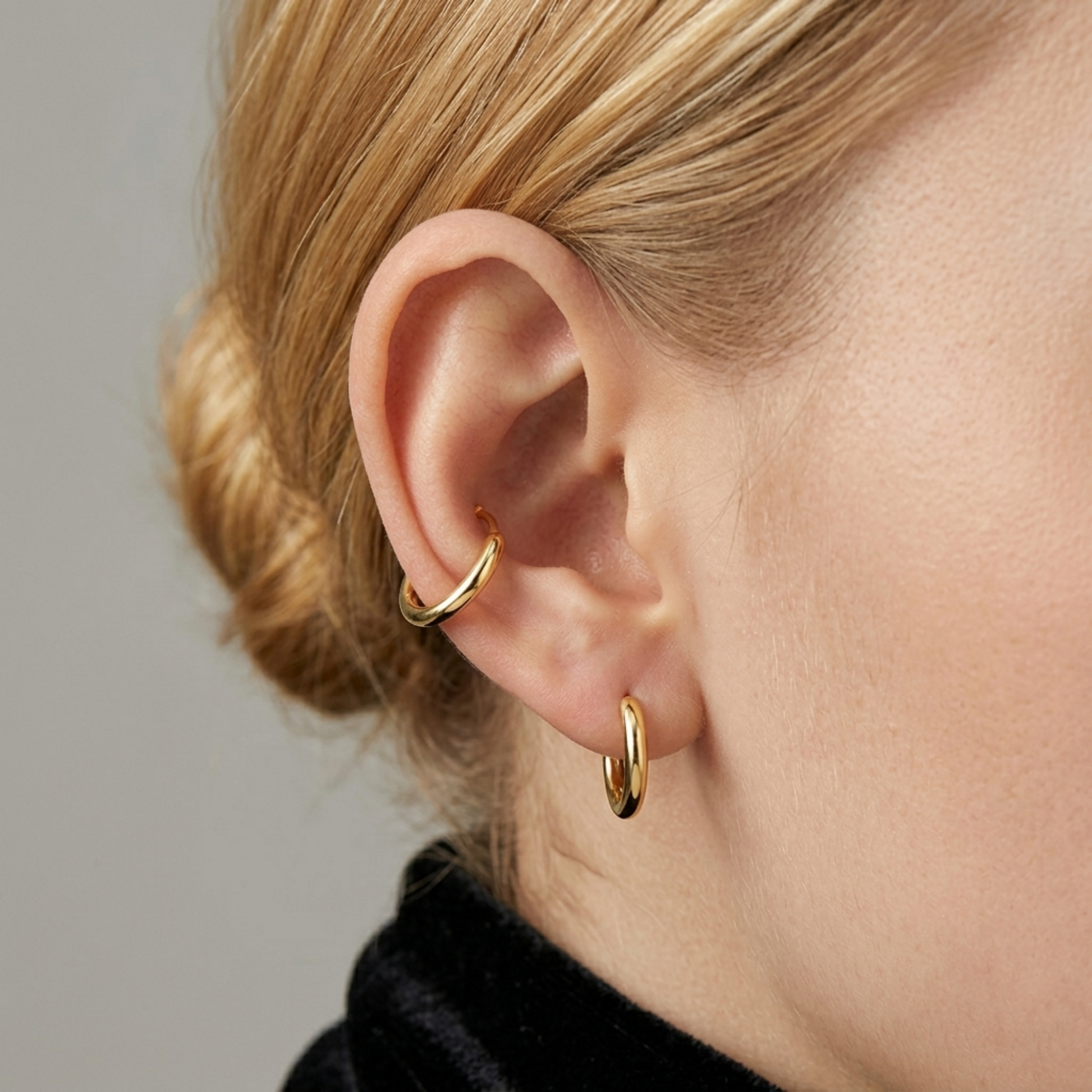 Gold-tone huggie hoop earrings on ear, small hoops stacked