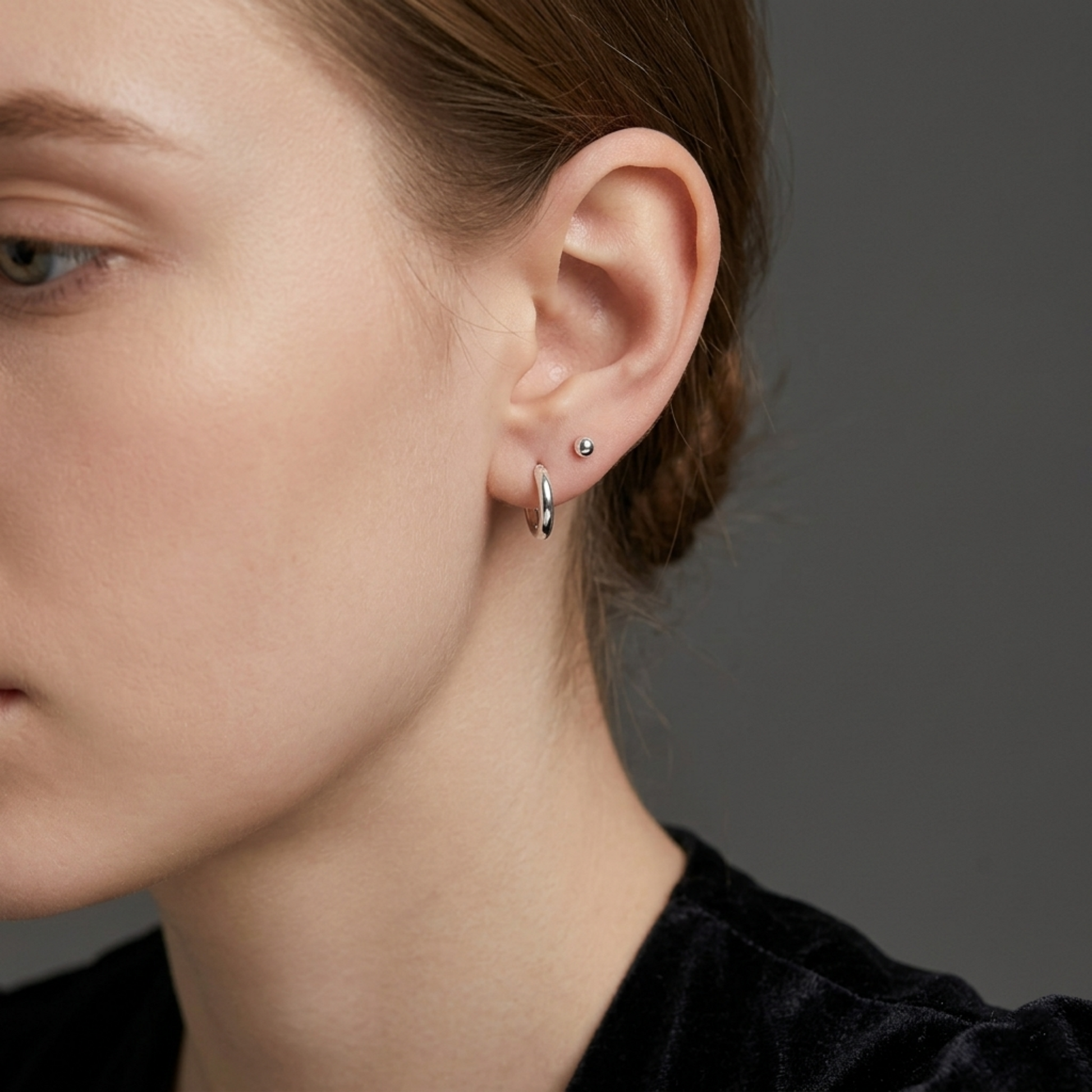 Rhodium-tone huggie hoop earrings on ear with small stud detail