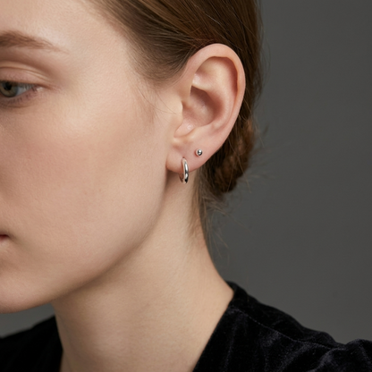 Rhodium-tone huggie hoop earrings on ear with small stud detail