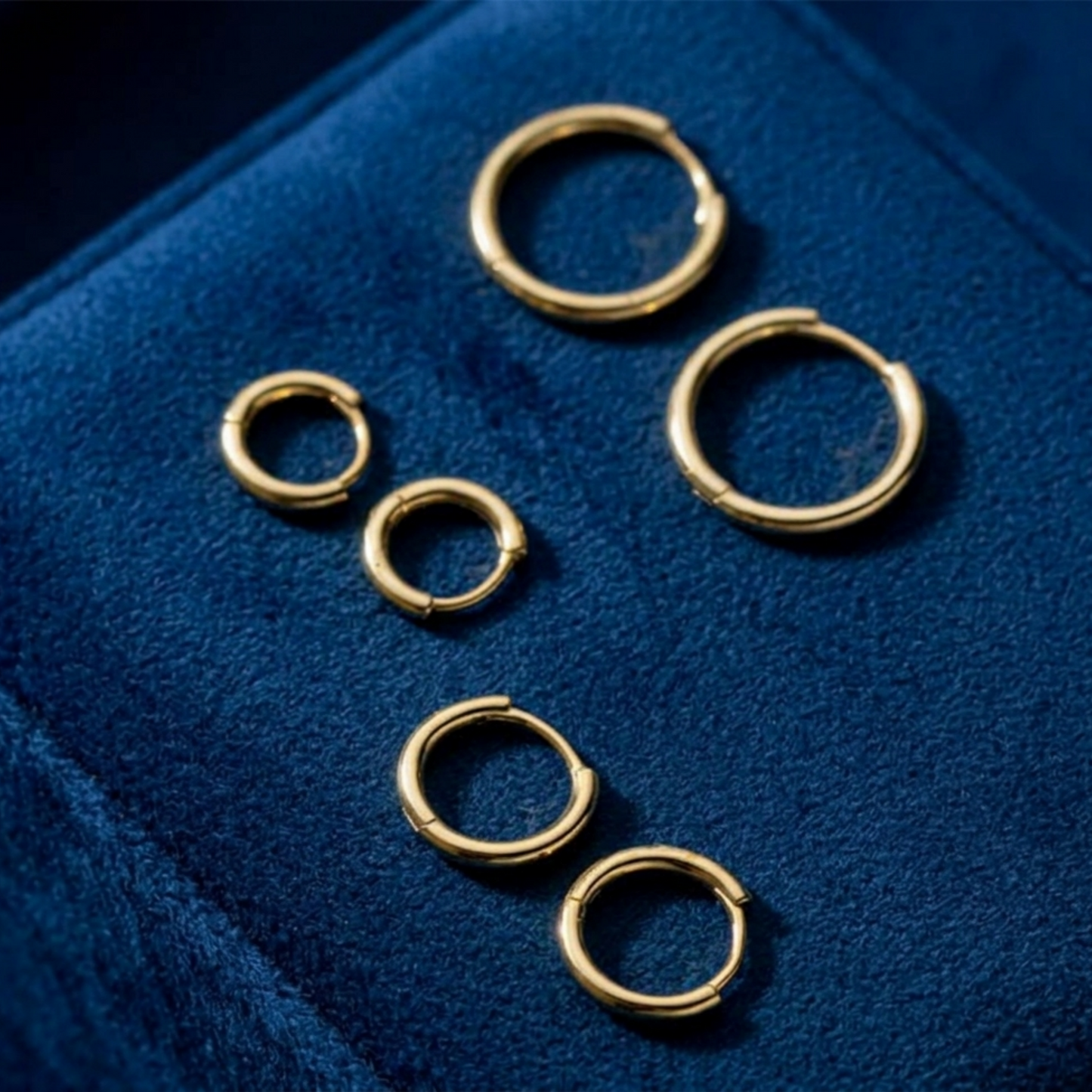 Gold-tone huggie hoop earrings, small hoops shown on a blue display