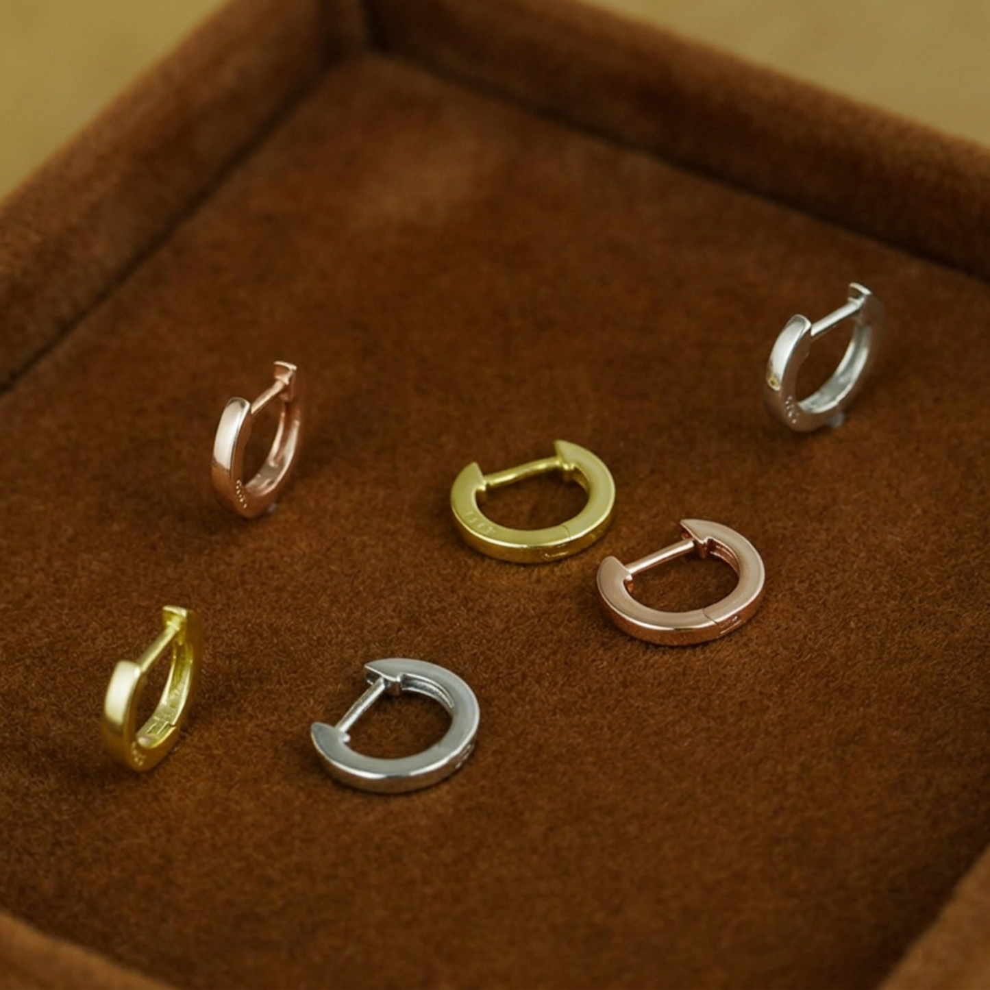 Assorted latch-back hoop earrings laid in a jewelry box, multiple metal tones