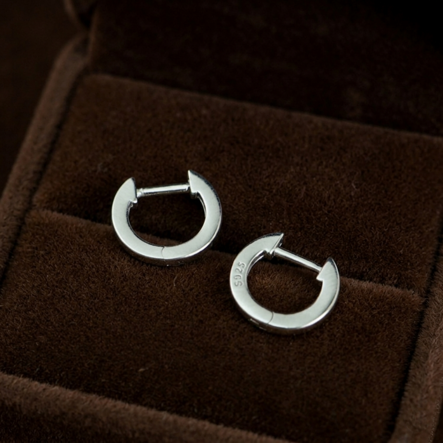 Silver latch-back hoop earrings, close-up on a dark jewelry box