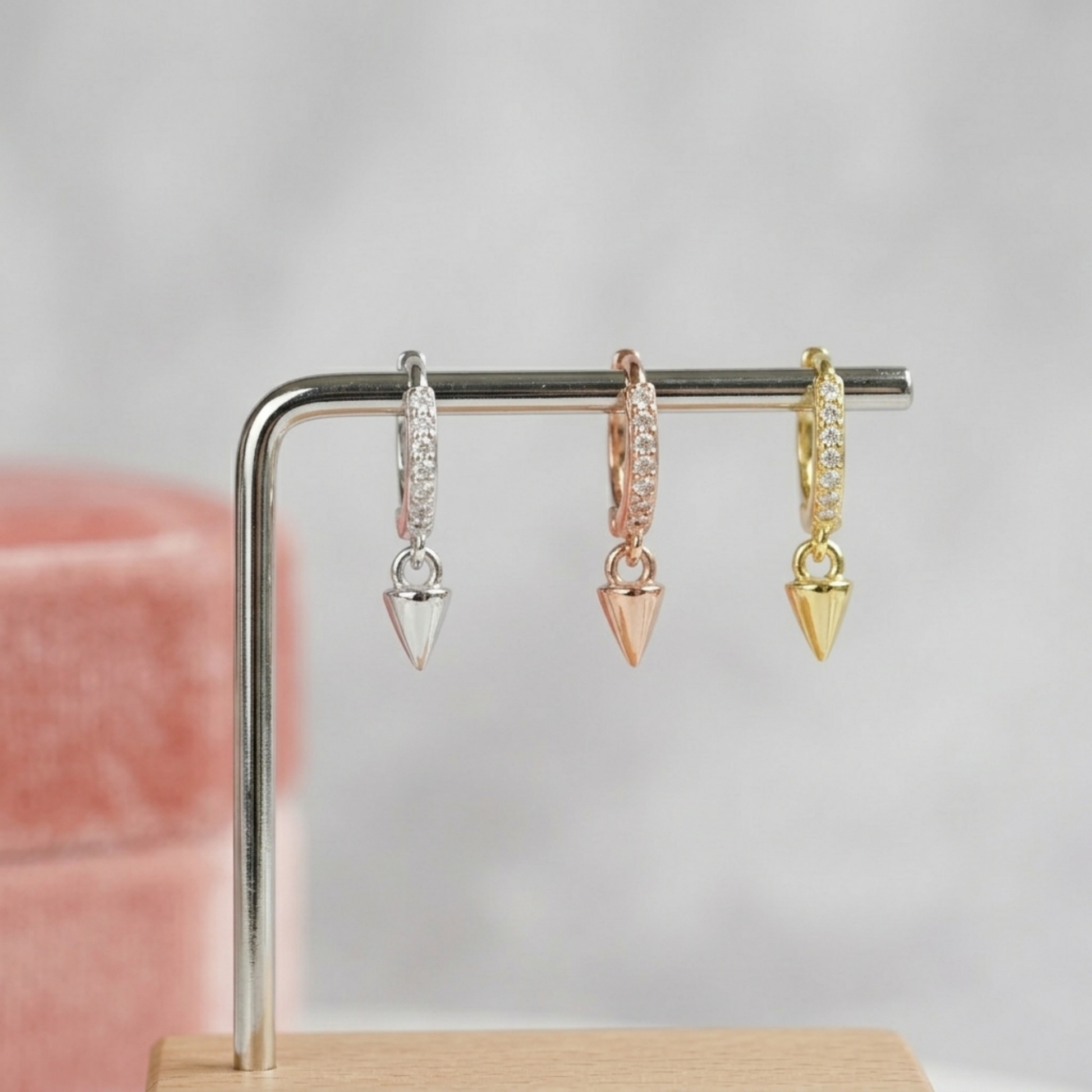 Cone-spike hoop earrings in silver, rose gold, and gold hanging on a bar