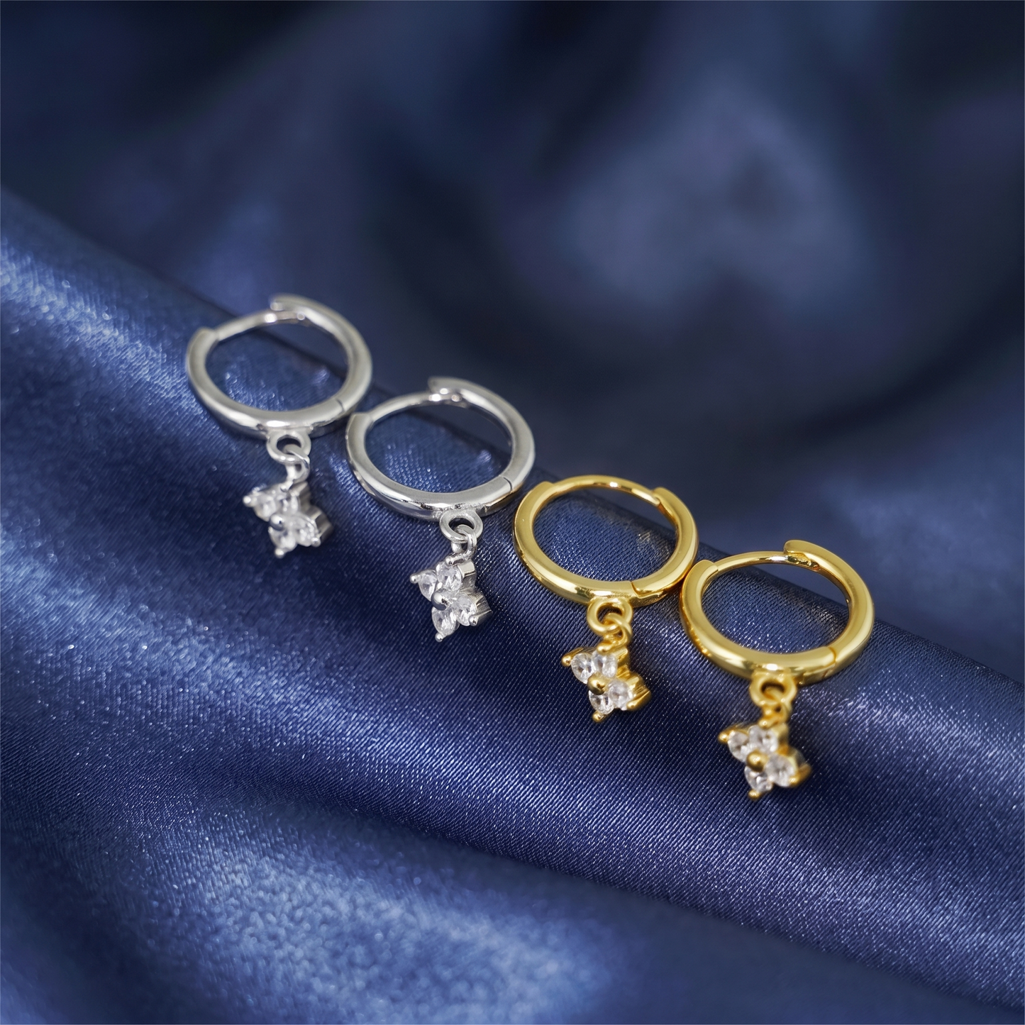 Silver and gold huggie hoop earrings with four-petal flower charms and crystals