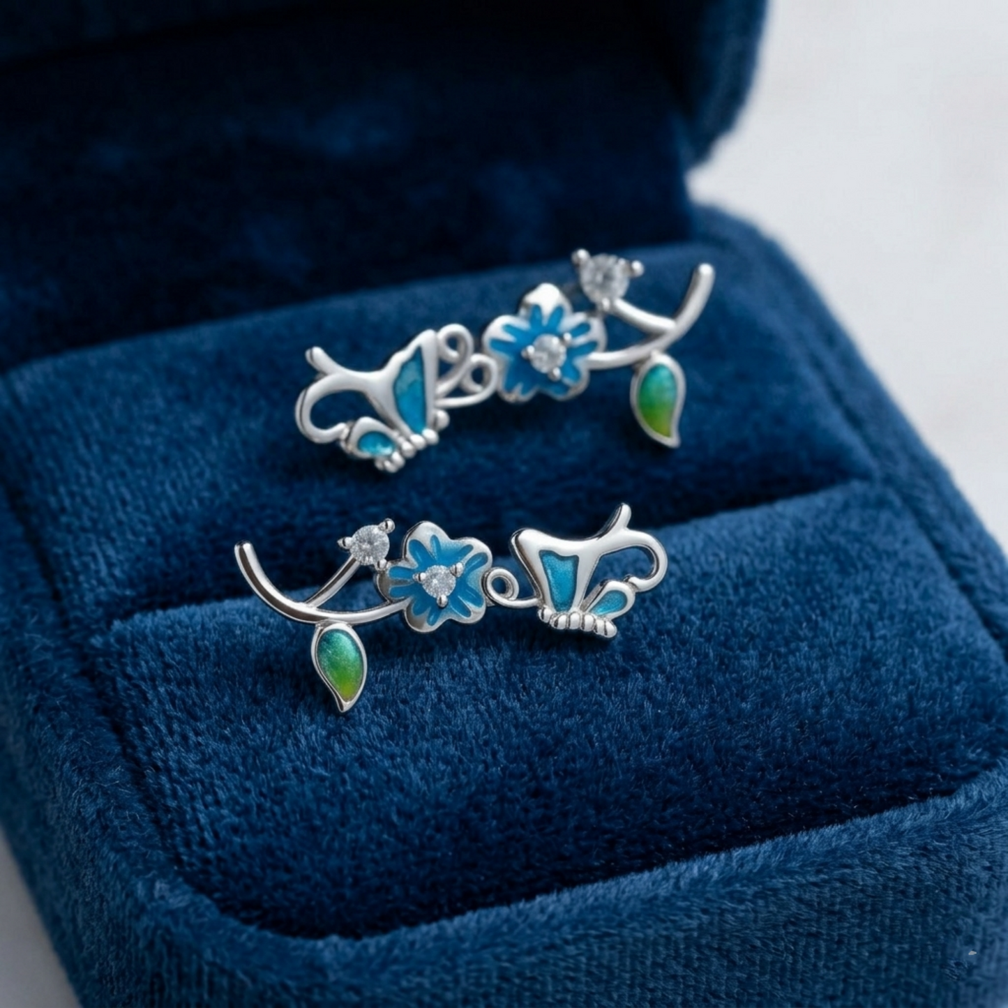 Silver butterfly climber earrings on blue velvet, blue enamel flowers and green drops