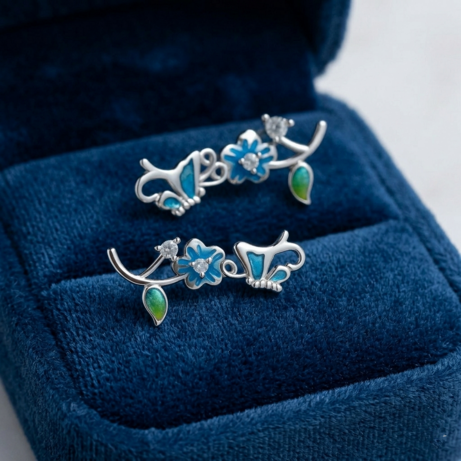 Silver butterfly climber earrings on blue velvet, blue enamel flowers and green drops