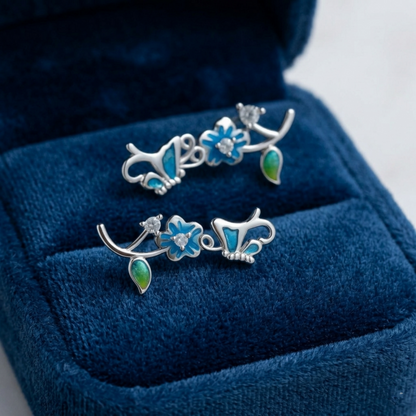 Silver butterfly climber earrings on blue velvet, blue enamel flowers and green drops