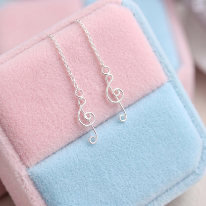 Silver treble-note threader dangle earrings resting on pastel pink and blue fabric