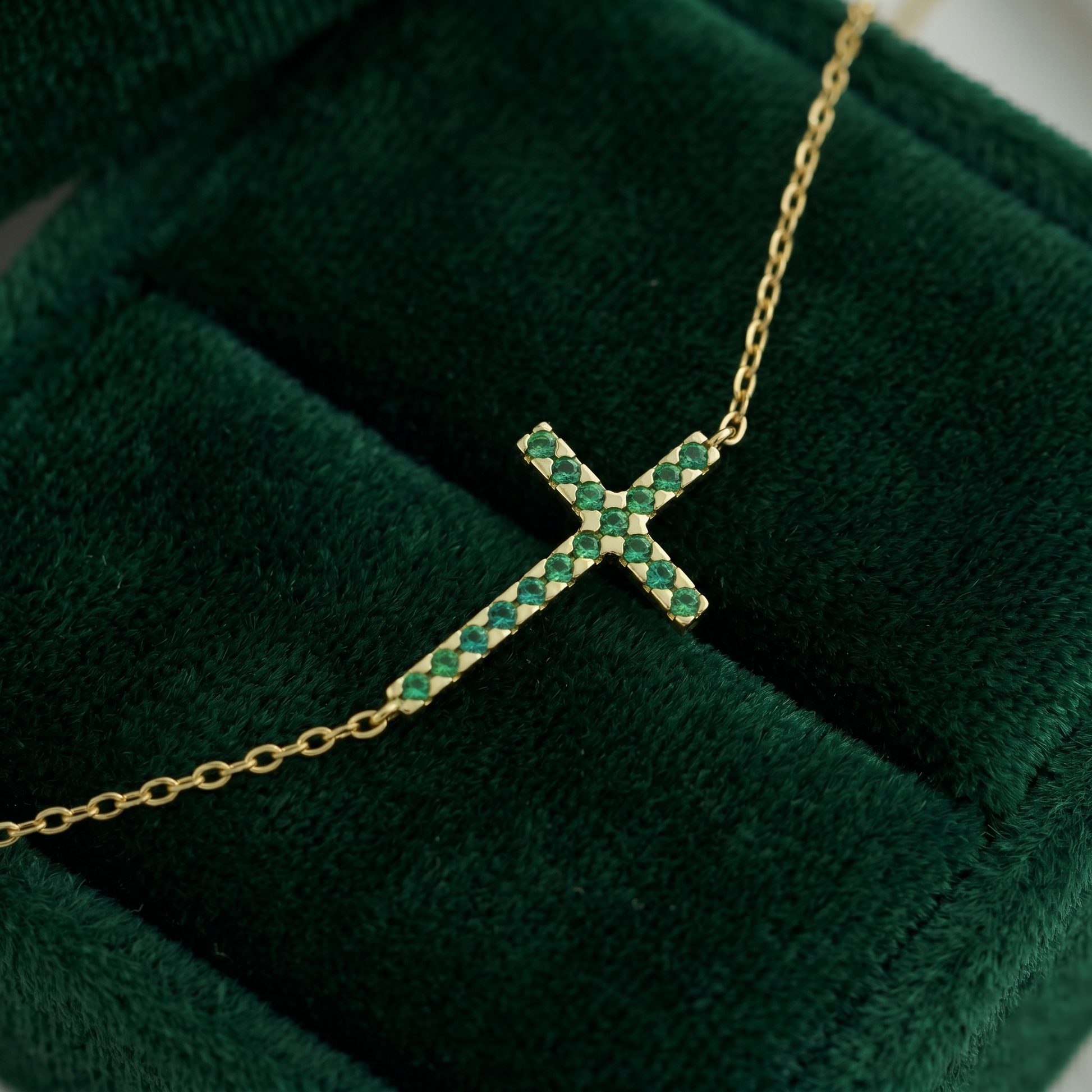 Gold-tone cross necklace with green crystal stones and fine chain, angled close-up