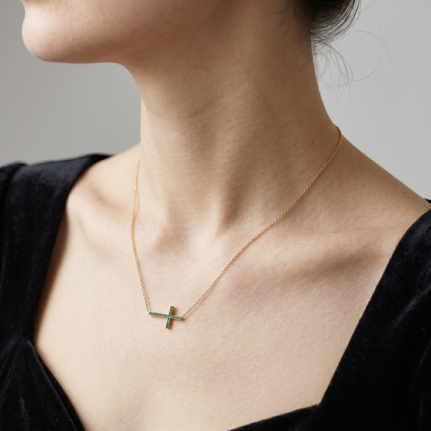 Gold-tone cross CZ necklace with green stones, worn on a fine chain, side view