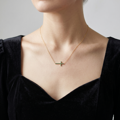 Gold-tone cross CZ necklace with green stones on a neckline, worn on a chain