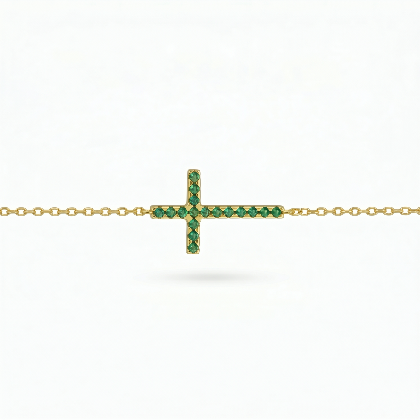 Gold-tone cross necklace with green crystal stones on a chain, side view