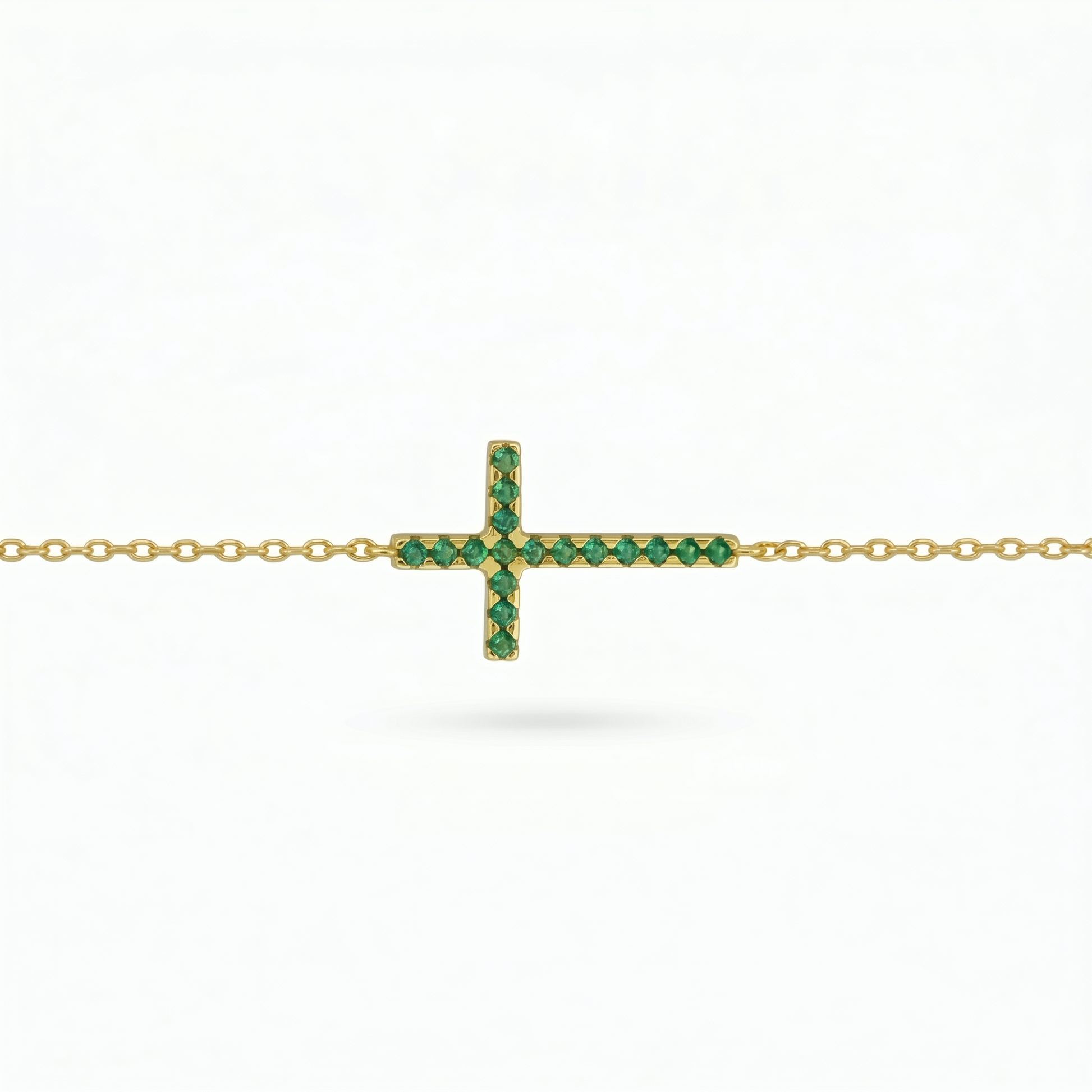 Gold-tone cross necklace with green crystal stones on a chain, side view