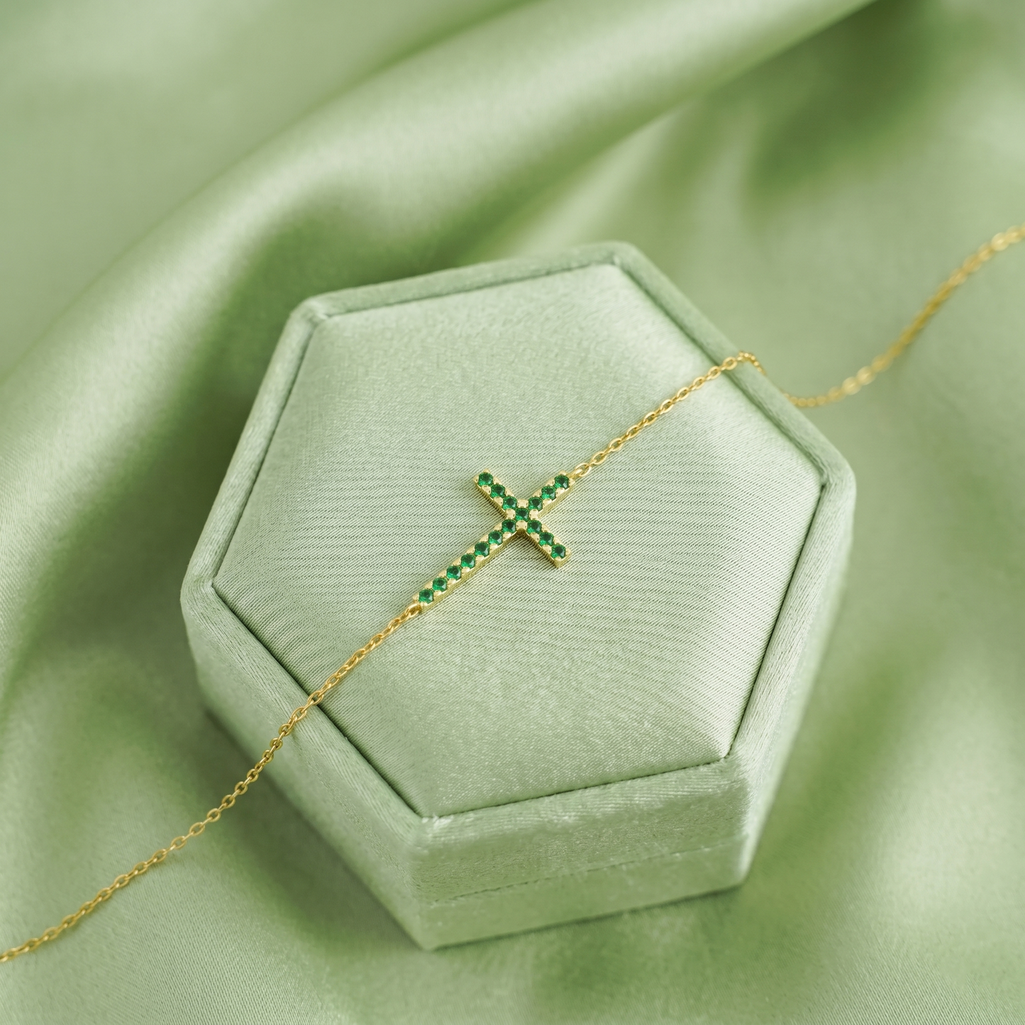 Gold-tone cross CZ necklace with green crystal stones, chain laid flat