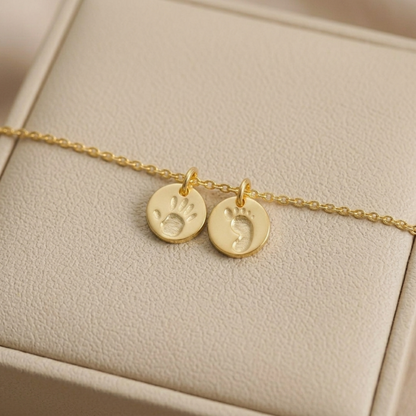 Gold round handprint and footprint charms on a thin chain