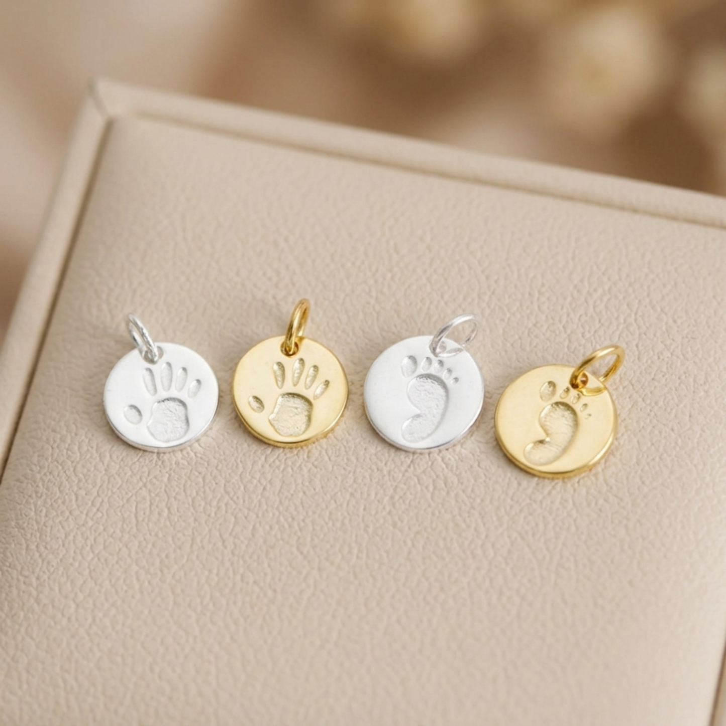 Round handprint and footprint charms set in silver and gold, on display card