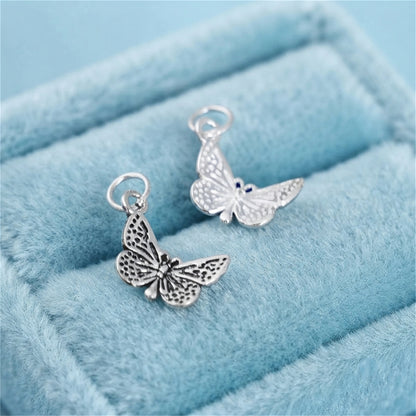 Silver butterfly charm pendant with scalloped wings on light blue velvet, close-up