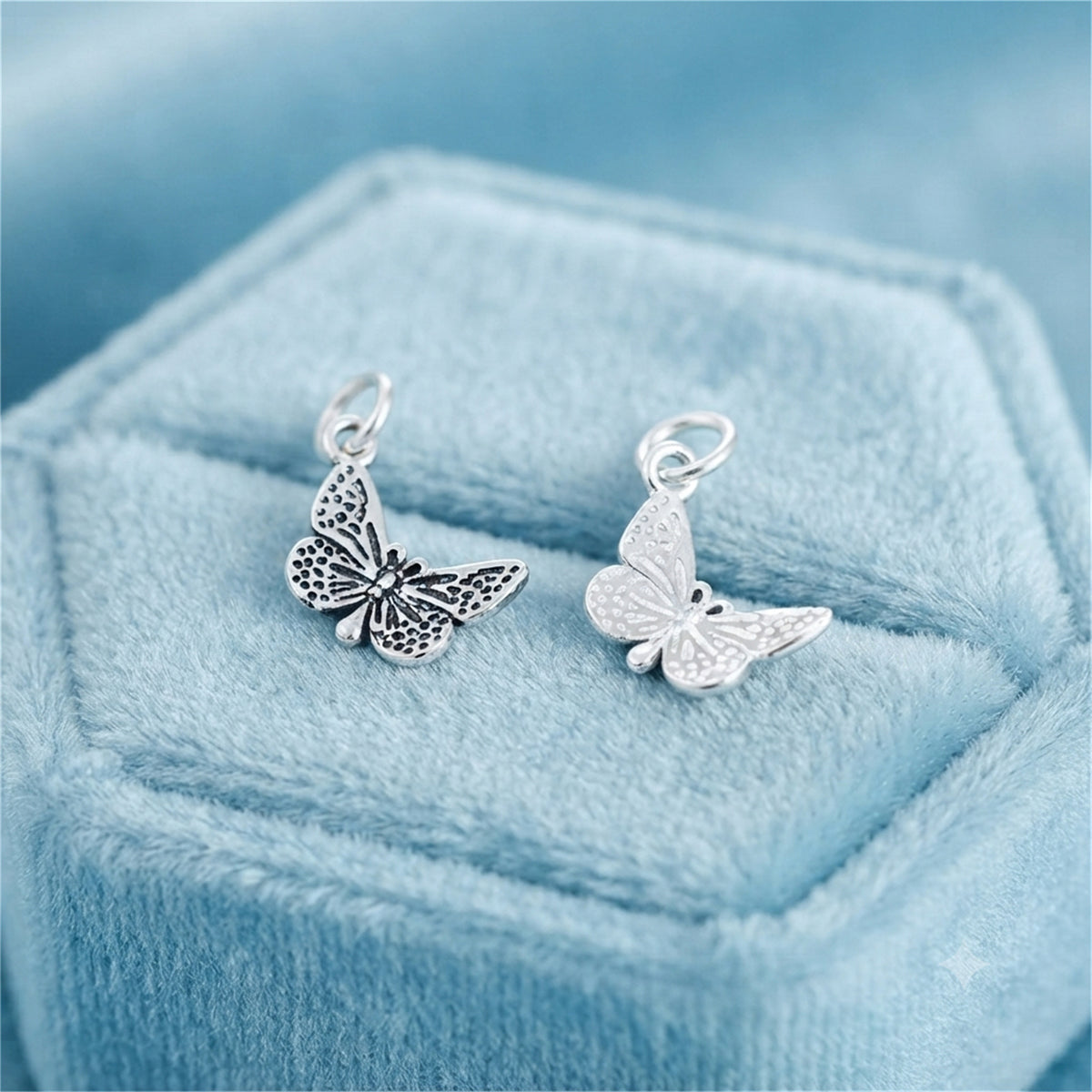 Silver butterfly charm pendant pair, two butterfly charms on light blue velvet