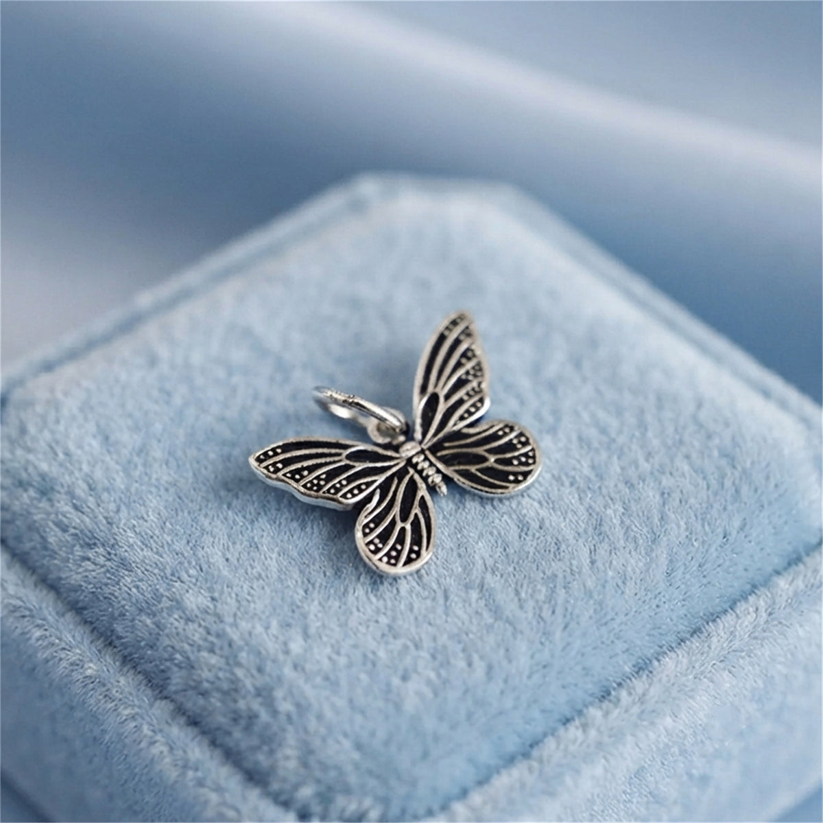 Silver butterfly charm pendant with black enamel accents, on light blue velvet