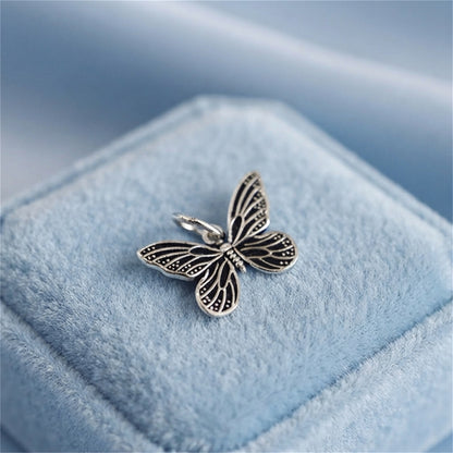Silver butterfly charm pendant with black enamel accents, on light blue velvet