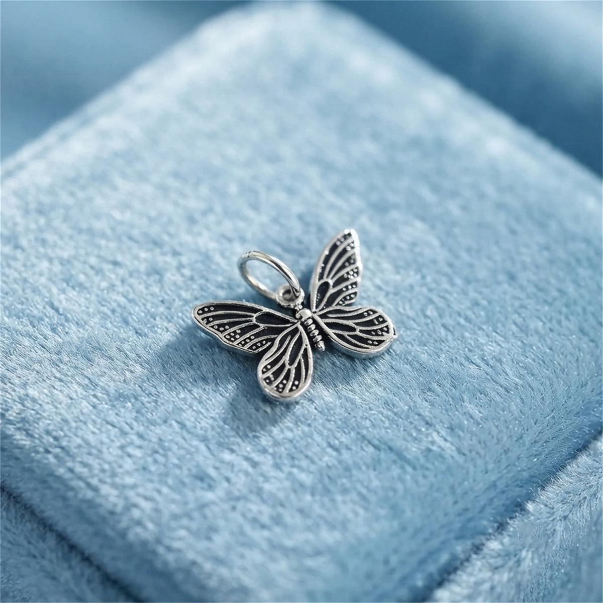 Silver butterfly charm pendant with filigree wings, loop bail on light blue velvet