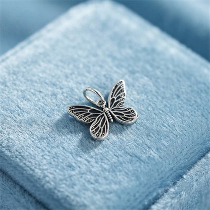 Silver butterfly charm pendant with filigree wings, loop bail on light blue velvet