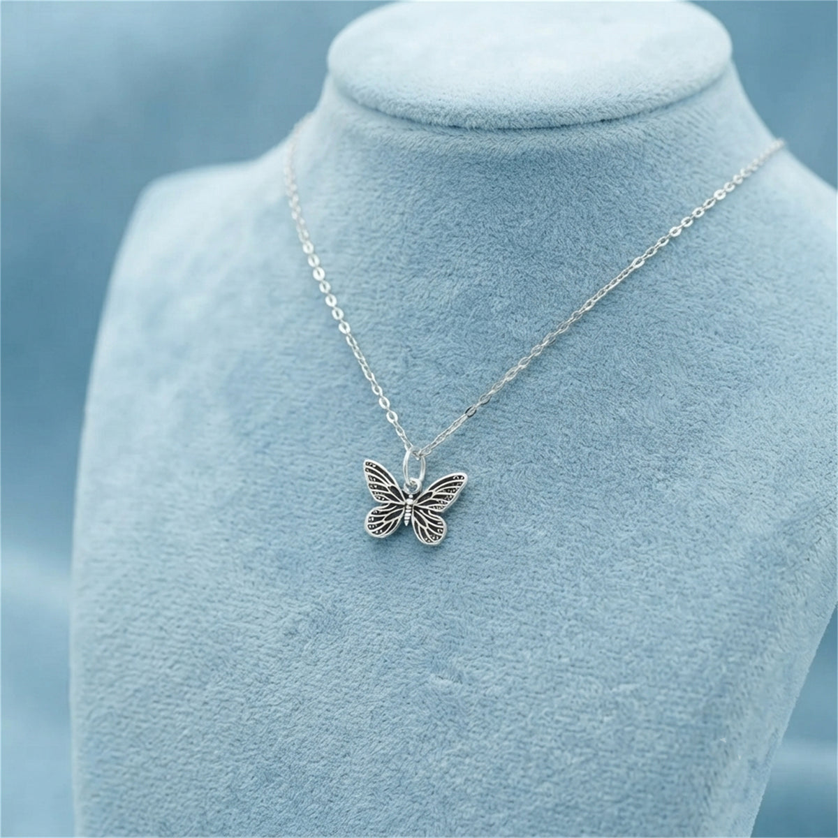 Silver butterfly charm pendant on a chain necklace, centered on display bust