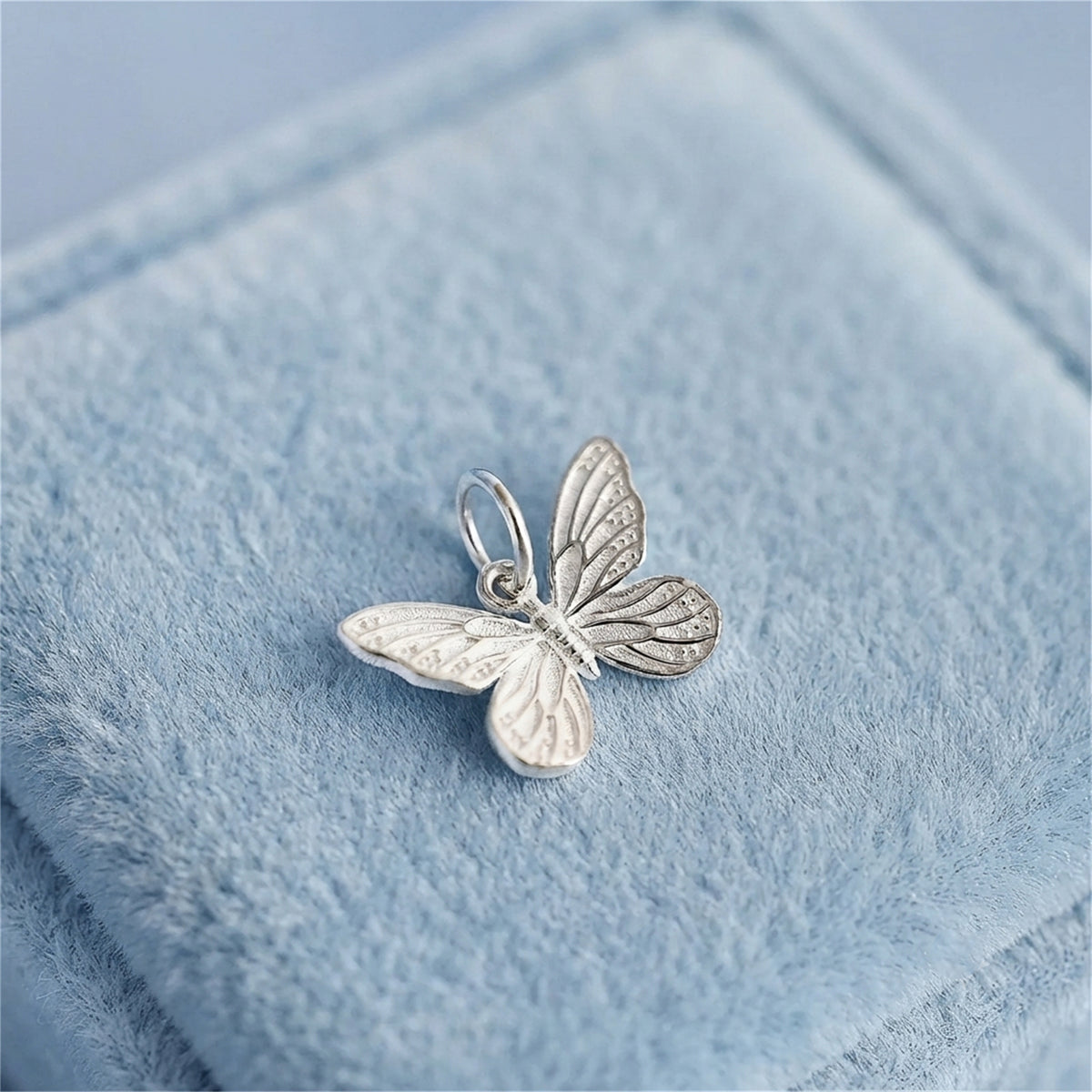 Silver butterfly charm pendant with detailed wings and loop bail on blue velvet