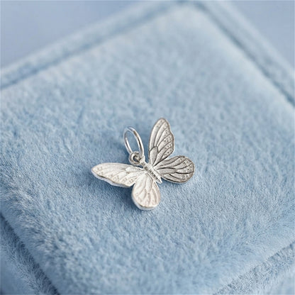 Silver butterfly charm pendant with detailed wings and loop bail on blue velvet