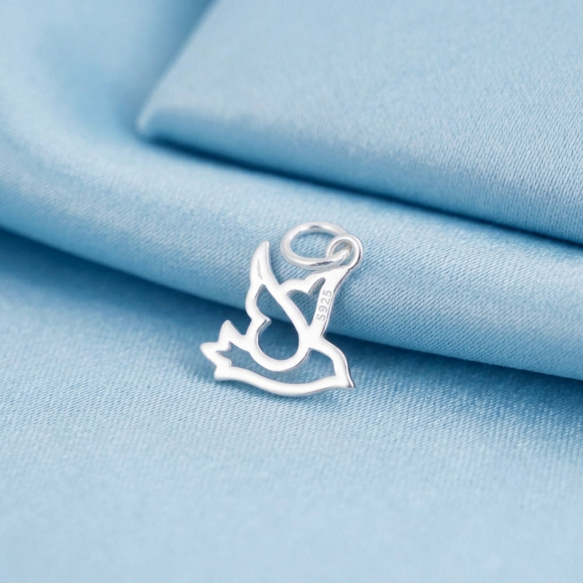 Silver dove peace charm with loop bail, resting on light blue fabric