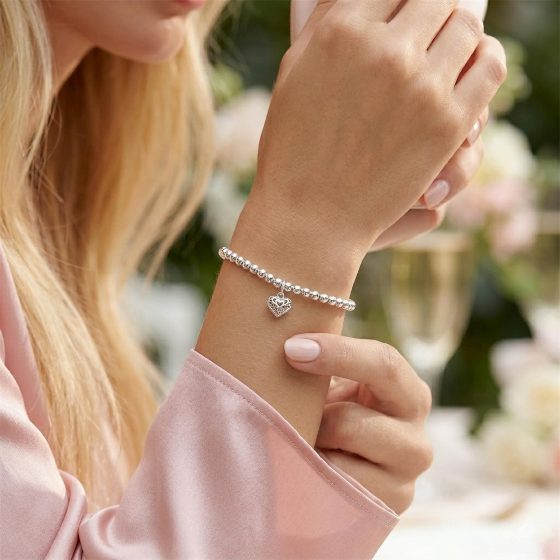 Filigree heart charm bracelet on wrist with delicate silver chain