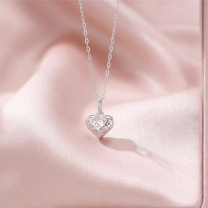 Filigree heart pendant necklace lying on pink fabric