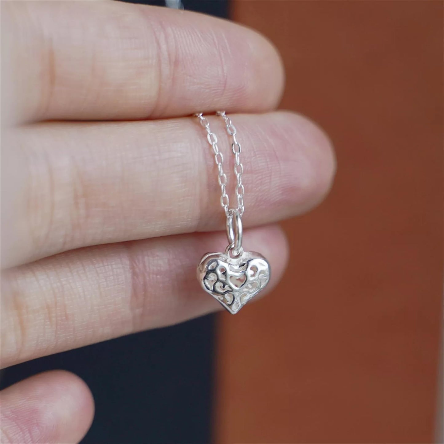 Filigree heart pendant on silver chain held in hand