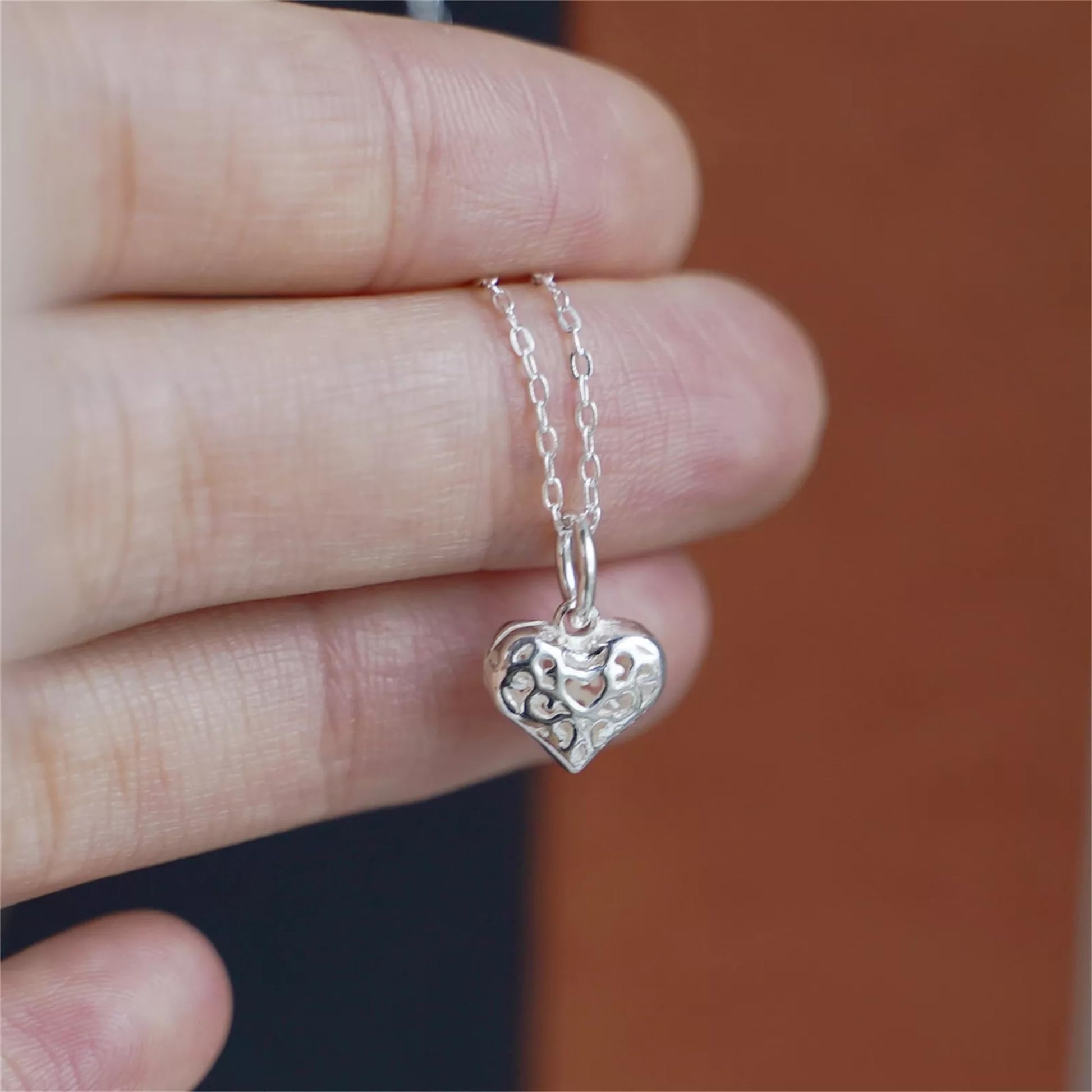 Filigree heart pendant on silver chain held in hand