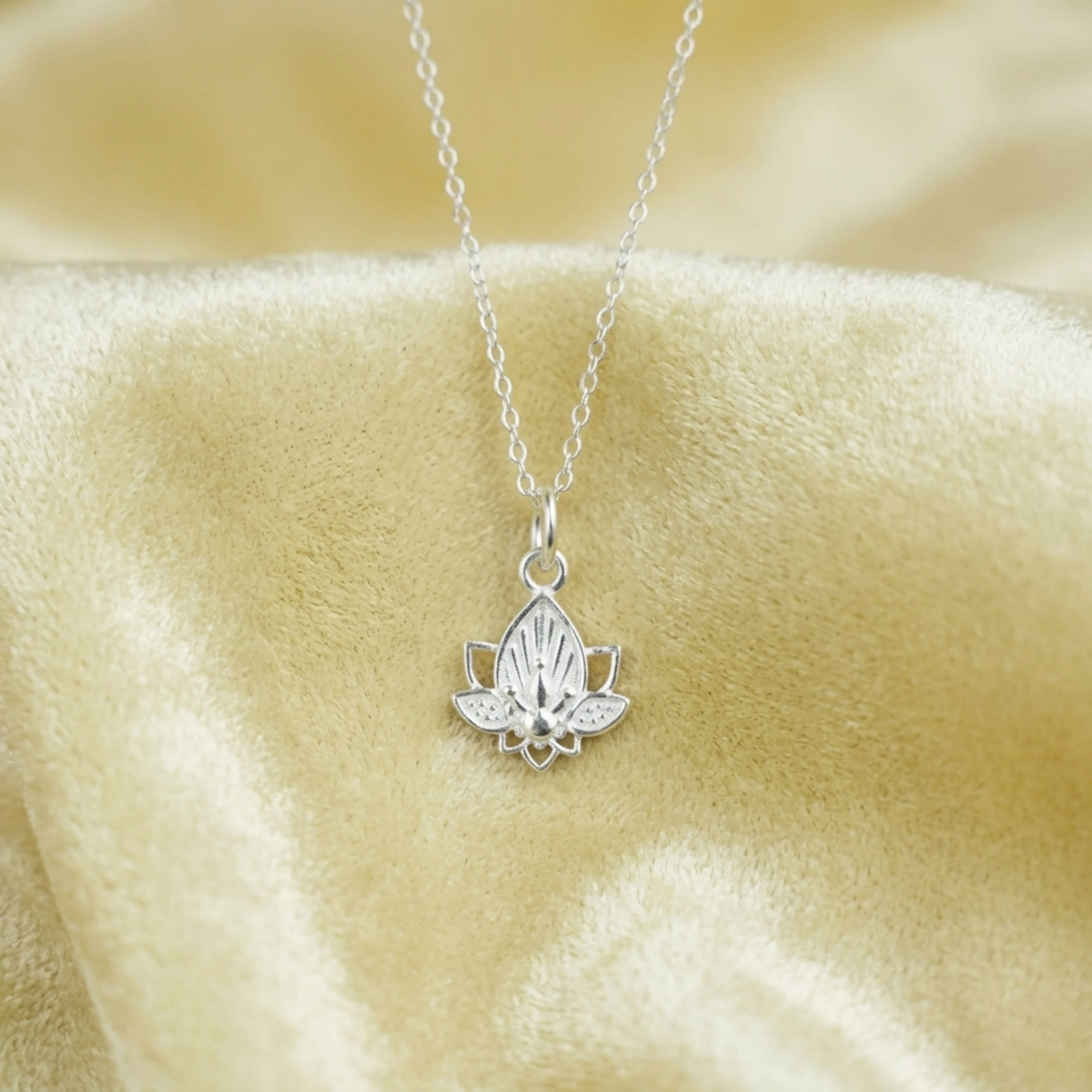 Lotus flower charm necklace with silver chain and single lotus pendant on soft fabric