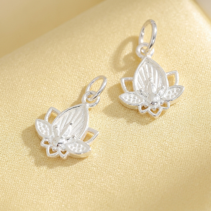 Lotus flower charm earrings in silver tone on light fabric, shown as two lotus drops