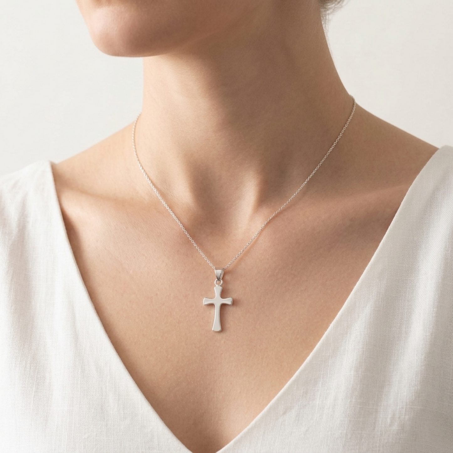 Cross pendant on a fine chain, worn on the neck over a light V-neck top