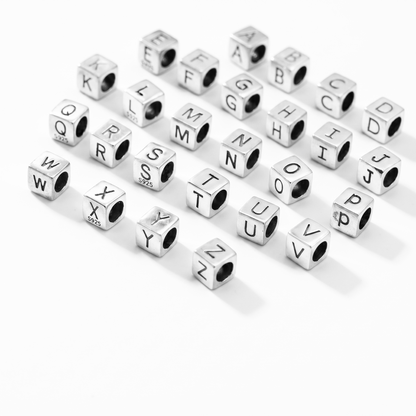 Silver alphabet cube beads scattered, showing embossed letters A to Z on cubes