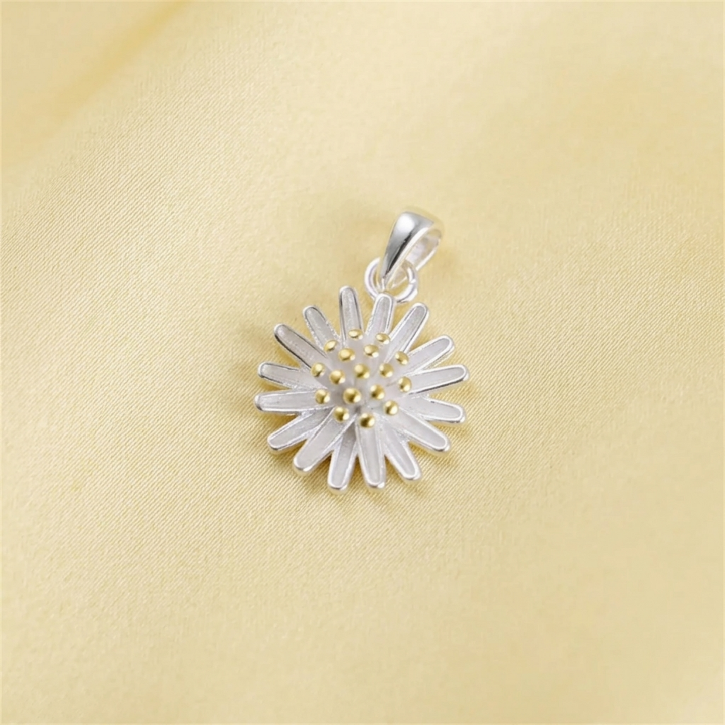 Silver daisy flower pendant on pale fabric, gold center and petal details