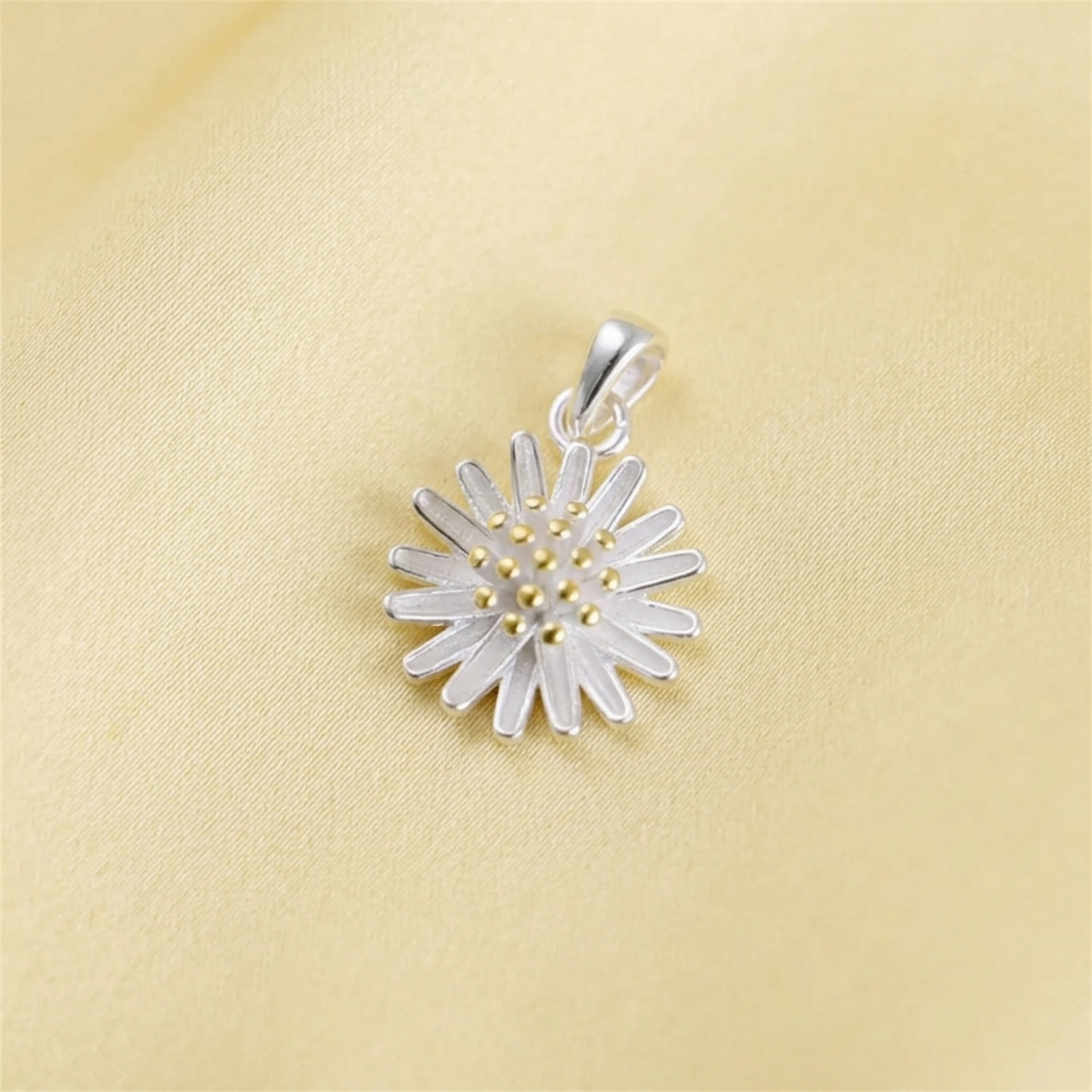 Silver daisy flower pendant on pale fabric, gold center and petal details