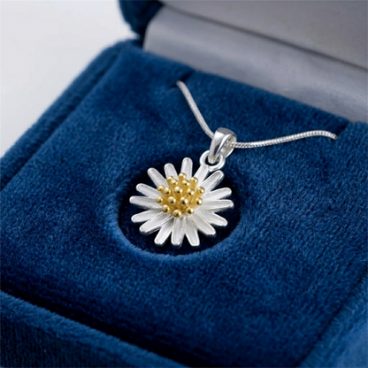 Silver daisy flower pendant with gold center on blue velvet display