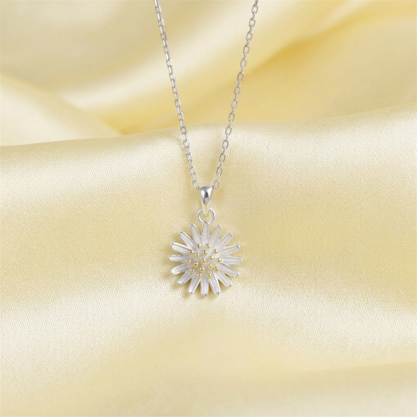 Silver daisy flower pendant necklace with chain and gold center on pale fabric